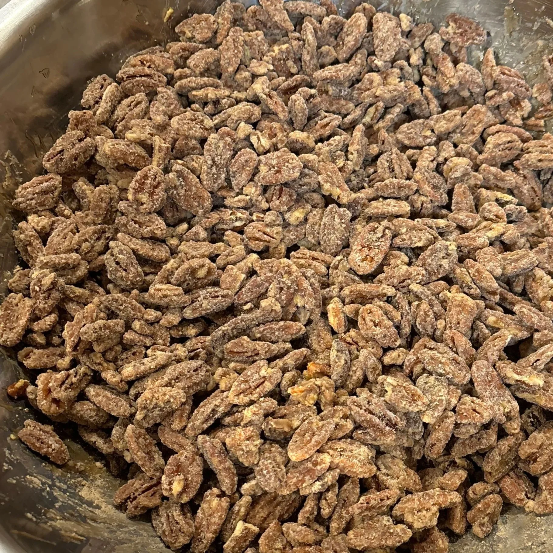 A close-up image of sweet, candied pecans in a stainless steel bowl, showcasing their crunchy texture and sugary coating.