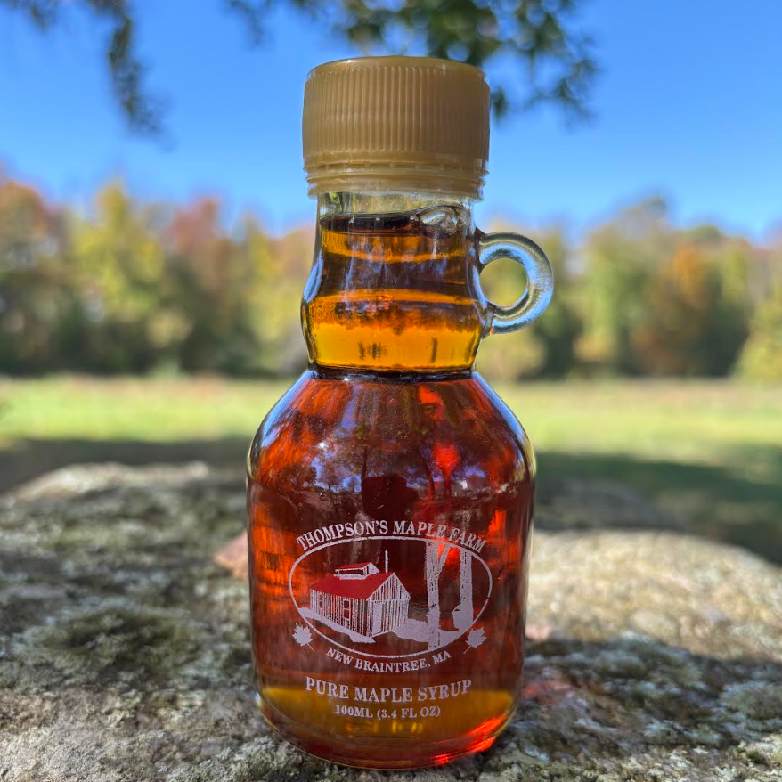 Bottle of Thompson's Maple Farm pure maple syrup set against a blurred natural background, showcasing the 100ml glass container with a classic design and gold cap. Ideal for enhancing breakfast dishes and desserts.