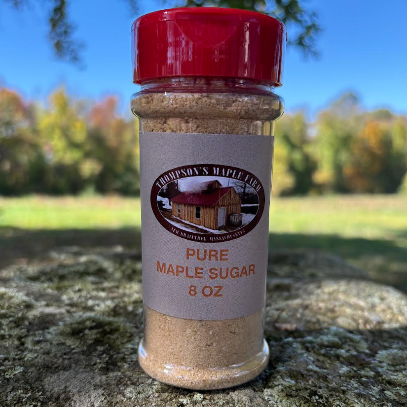 8 oz jar of Thompson's Maple Farm pure maple sugar, featuring a rustic label with an illustration of a maple syrup house, set against a natural outdoor background with colorful foliage. Perfect for baking, cooking, or sweetening beverages.