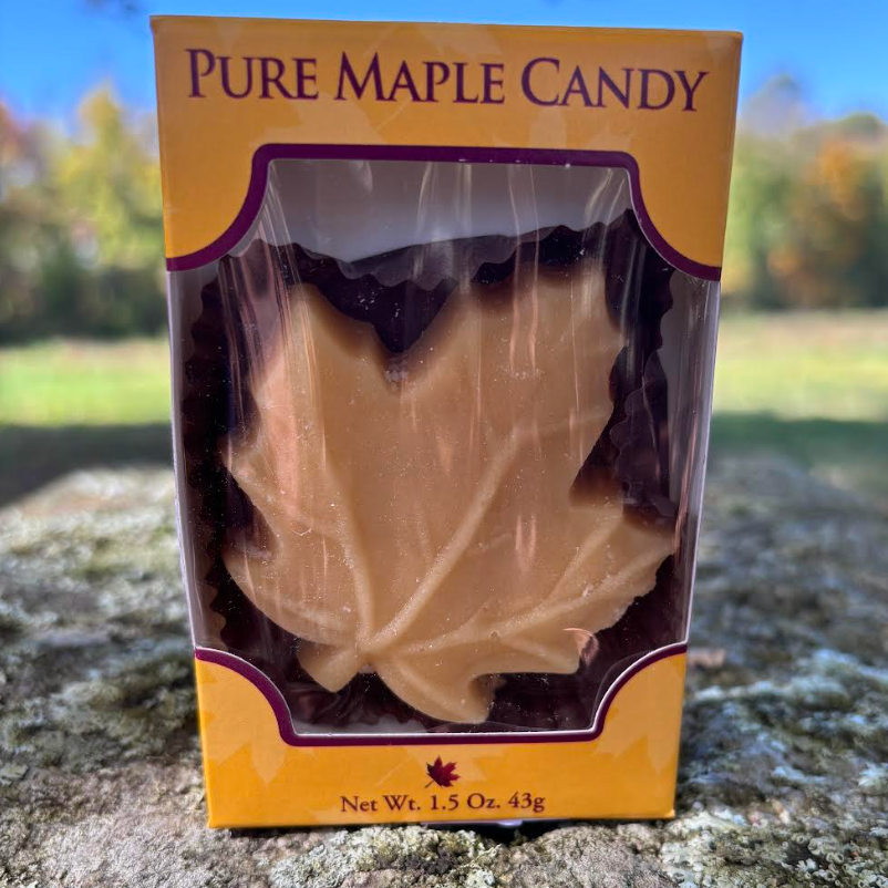 Pure maple candy shaped like a maple leaf, packaged in a colorful box with a net weight of 1.5 ounces (43g), set against a blurred natural background.